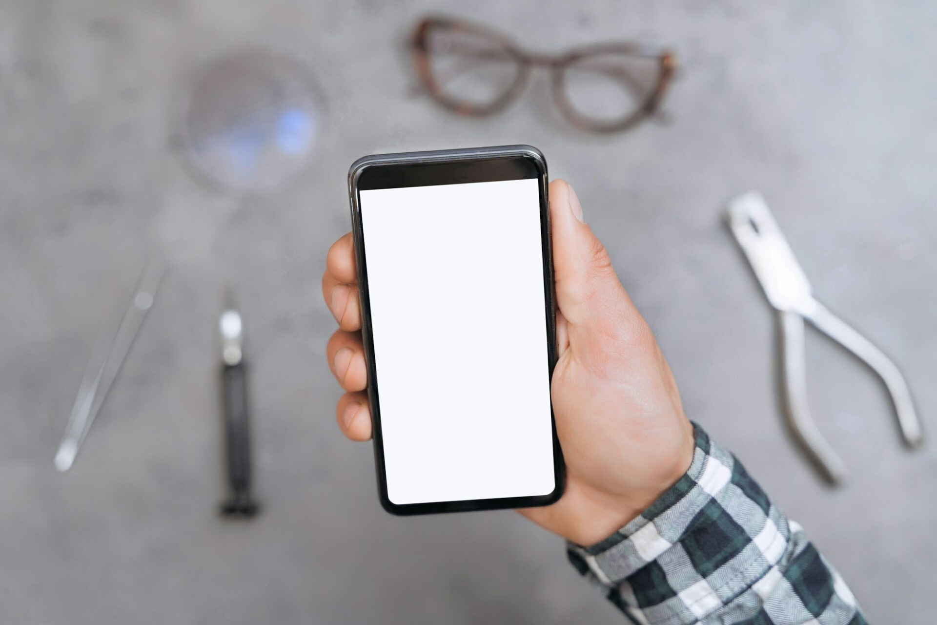 Closeup of cellphone with blank screen in man's hand in optical workshop