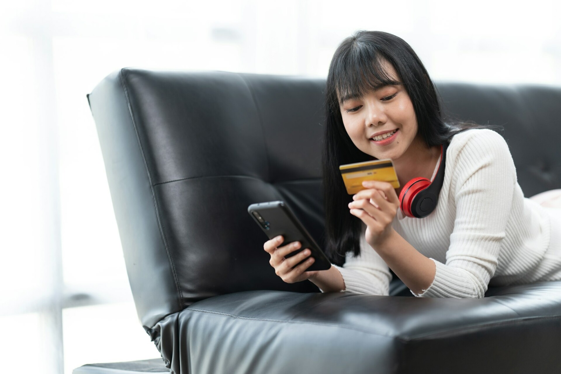 Young confident pretty woman working with smartphone and credit card at home.